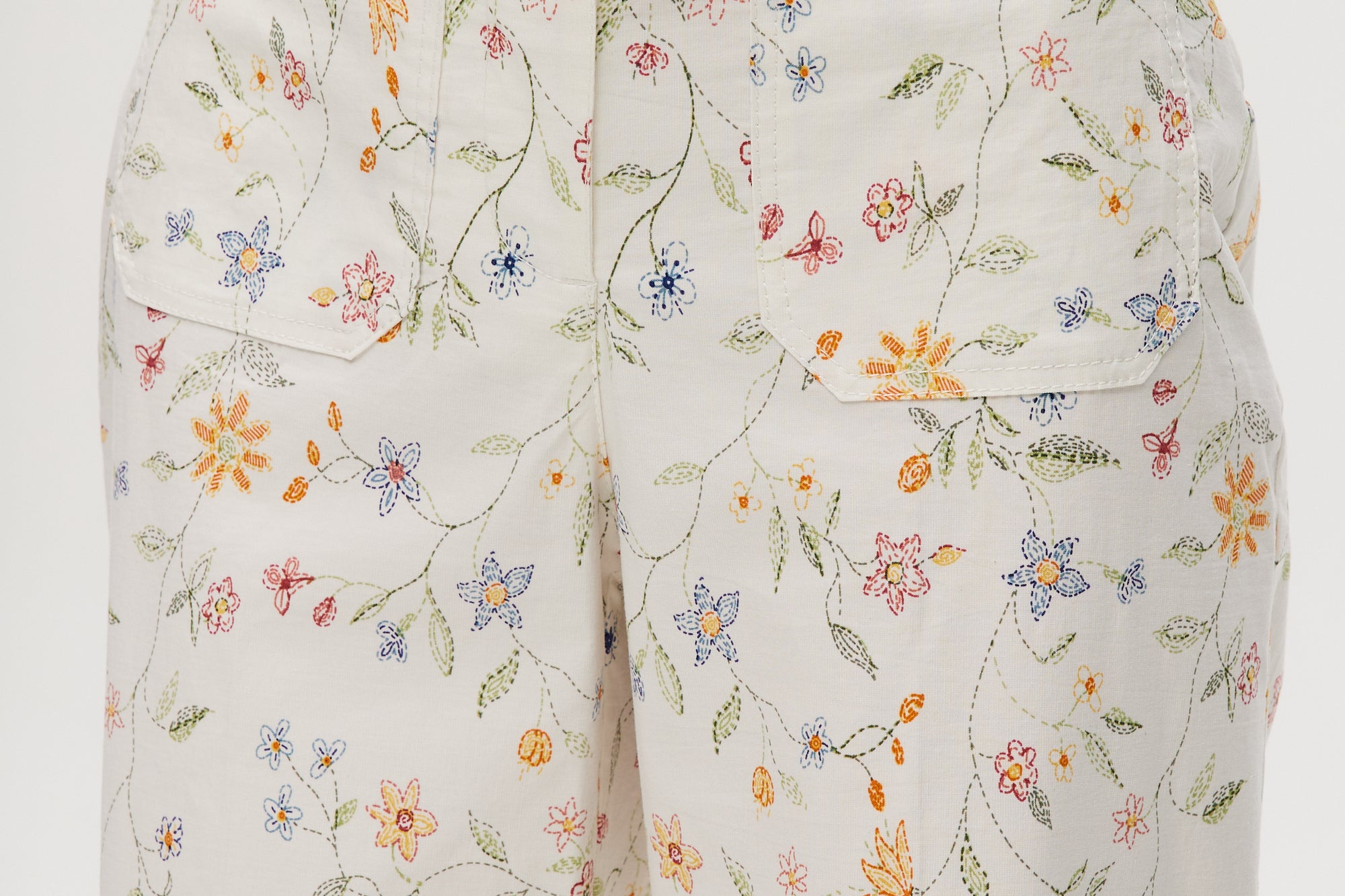 White high-rise straight leg pants with floral print, featuring a button-front closure and pockets by Hilary Radley.