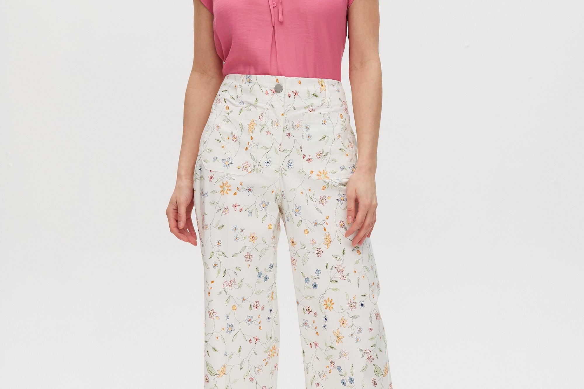 White high-rise straight leg pants with floral print, featuring a button-front closure and pockets.