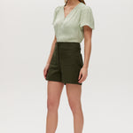 Olive high-rise stretch shorts featuring button closure, front patch pockets, and textured fabric by Hilary Radley.