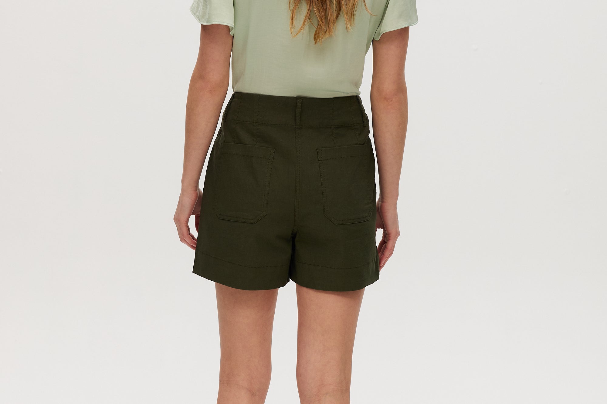 Olive high-rise stretch shorts featuring button closure, front patch pockets, and textured fabric by Hilary Radley.