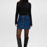 Blue denim mini skirt with contrast vegan leather trim and gold buttons.