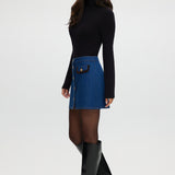 Blue denim mini skirt featuring contrast vegan leather trim and gold buttons by Hilary Radley.