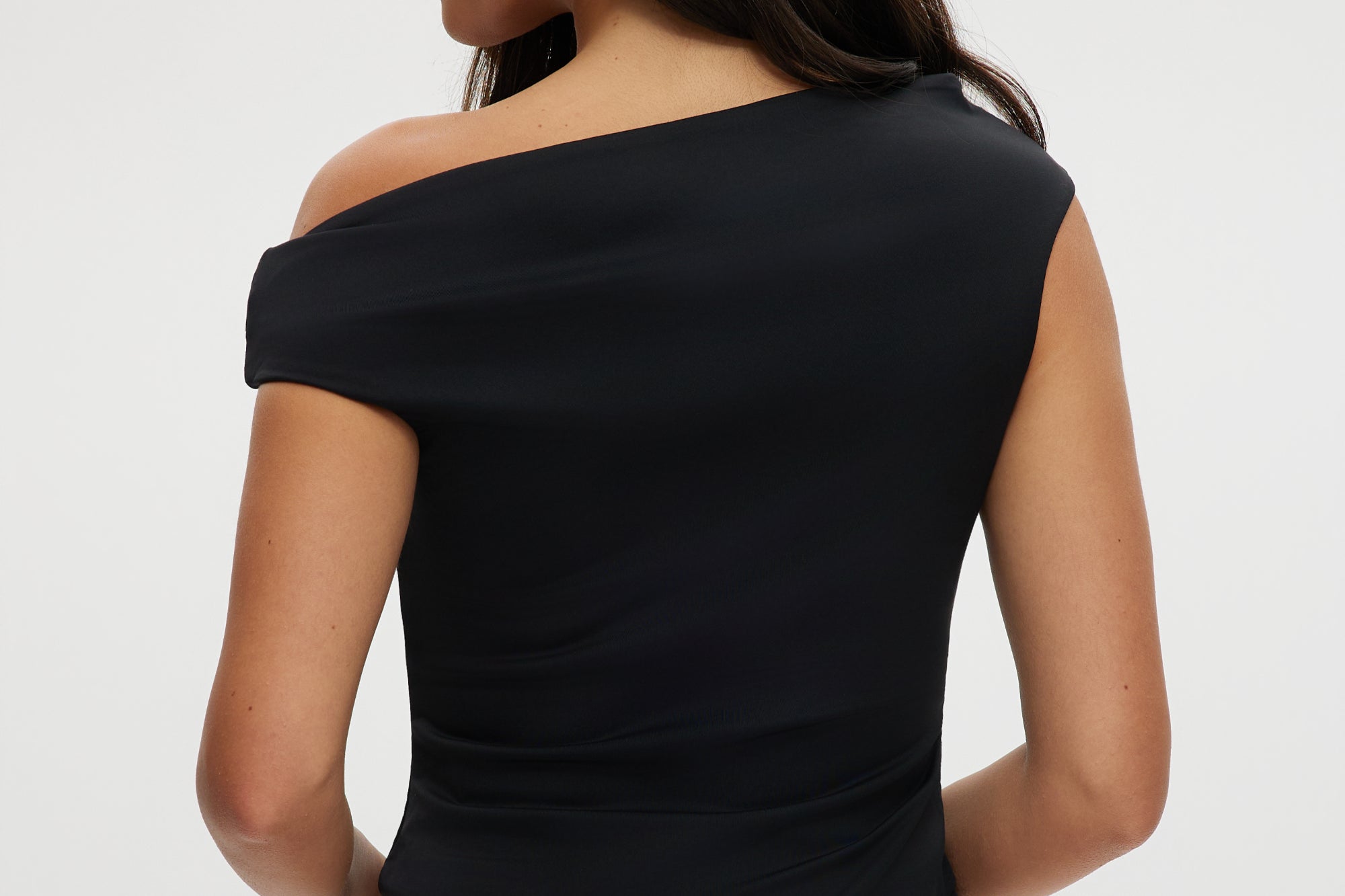 Black asymmetrical one-shoulder top featuring gold detail, available from Hilary Radley.