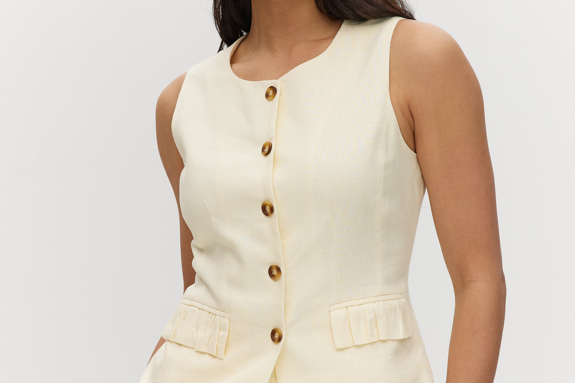 Light cream sleeveless top with button-front and waist tab detail.