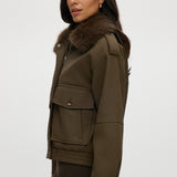 Olive coated jacket featuring a removable faux fur collar, flap pockets, and ribbed hems by Hilary Radley.