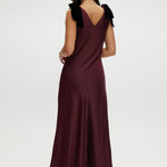 Bordeaux satin maxi dress with velvet bow shoulder details, sleeveless design, and V-neckline.