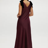 Bordeaux satin maxi dress with velvet bow shoulder details, sleeveless design, and V-neckline.